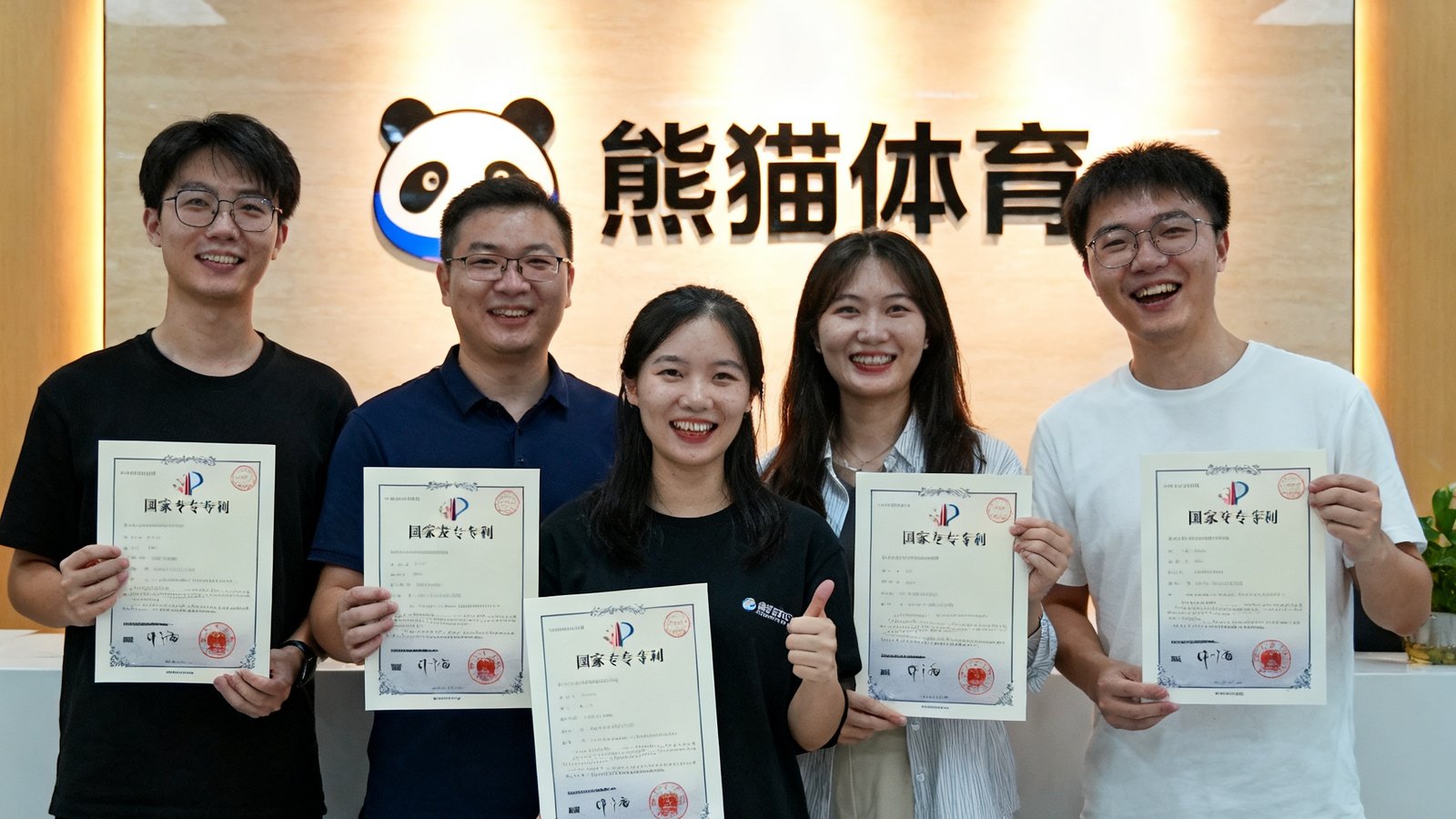 熊猫体育技术团队手持国家发明专利证书合影庆祝，背景为公司logo墙